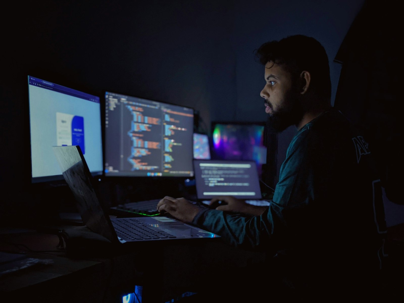 Engineer building software across three monitors at night